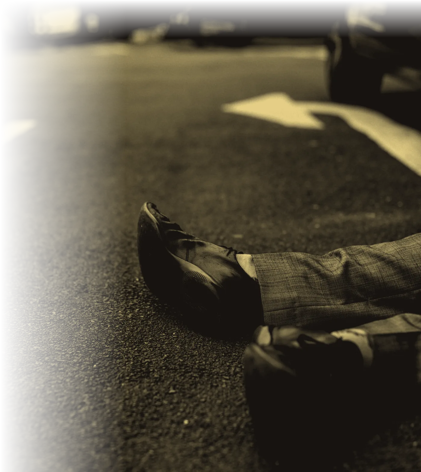 A pair of legs and dress shoes lying across a road beside a lane-marking arrow.